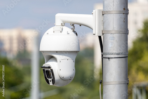 Modern white outdoor PTZ security camera mounted on a metal pole for city surveillance, high-tech dome CCTV system for public safety and monitoring in urban area