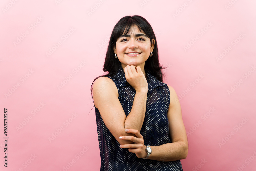 Obraz premium Smiling latina woman posing in studio against pink background, expressing happiness, confidence, and positive emotions