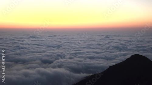 Sea of clouds from mountain peak at dawn, pastel sky over vast rolling mist blanket. Overcast carpet observed near summit before sunrise, warm gradient light across foggy expanse.
