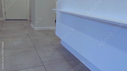 Interior hallway with white wall and tiled floor, showing gradual movement of a horizontal ledge along the wall in a modern setting