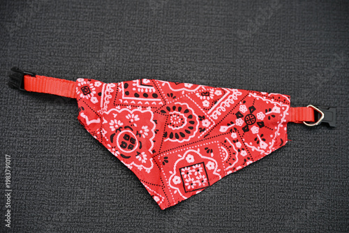 a red bandana-type scarf for dogs with a red paisley pattern and an adjustable collar.