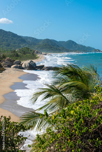 Scenic Caribbean coastline featuring sandy shore, rounded rock formations, turquoise sea, and green jungle hills
