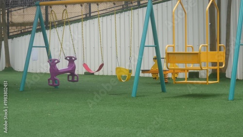 empty children's playground with various types of colorful swings on synthetic grass