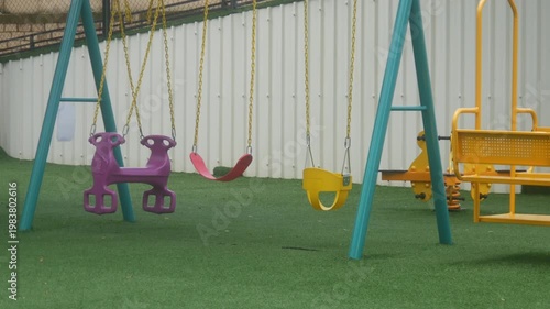 empty children's playground with various types of colorful swings on synthetic grass