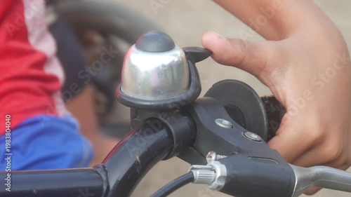 A child's hand is ringing the bell on the handlebars of a bicycle outdoors.
