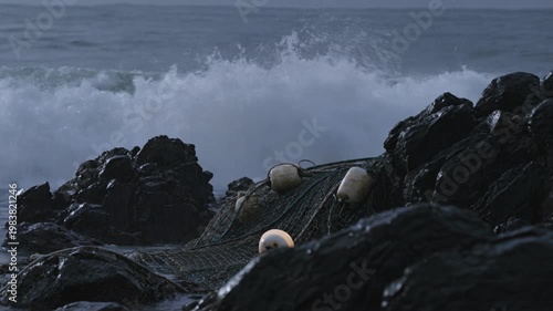 Fishing Net Snagged on Sharp Coastal Rocks Faces Heavy Rain and Waves Crashing Over Jagged Shores