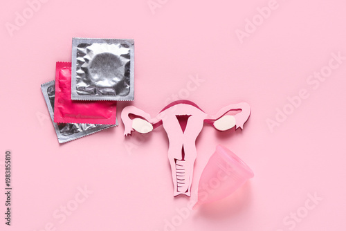 Paper uterus with condoms and menstrual cup on pink background