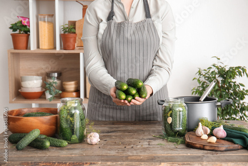Woman holding fresh cucumbers for canning at table in kitchen