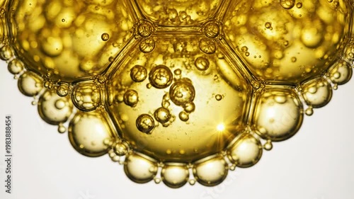 Extreme macro shot of golden yellow transparent bubbles of varying sizes clustered together, resembling viscous oil, honey, or serum with a bright light reflection and starburst effect.