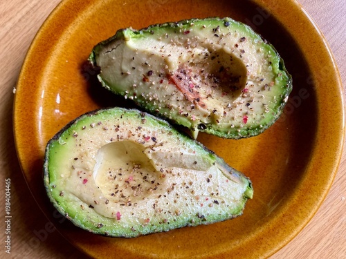 Avocado pear cut in half with black pepper and Himalayan pink salt