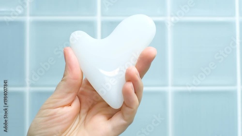 A hand holding gua sha face massager on blue background.