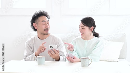 リビングでスマホを見て笑顔の日本人夫婦
