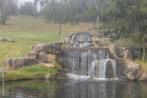 An on demand waterfall or cascade falling in three tiers or steps over rocks that have been placed to create this artificial waterfall at the arboretum in Armidale in New South Wales, Australia.