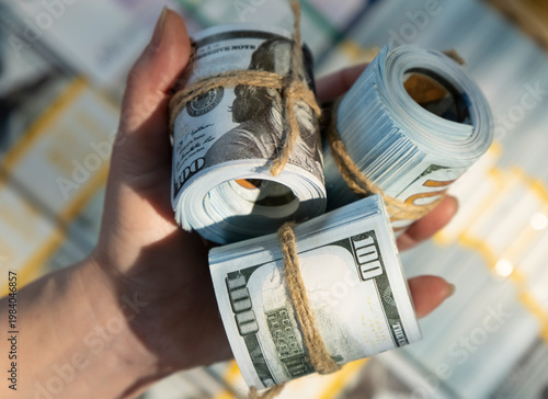 Hand holds rolled stacks of money tied with string on a table filled with more cash