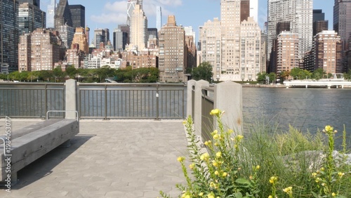 New York City Manhattan Midtown skyline from Roosevelt Island park, United States. Red brick buildings architecture, riverside cityscape near East River water, Turtle Bay residential houses and bench.