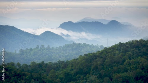 Time lapse video of mist or fog flowing through a valley there are lines of electrical transmission towers high on the mountain.