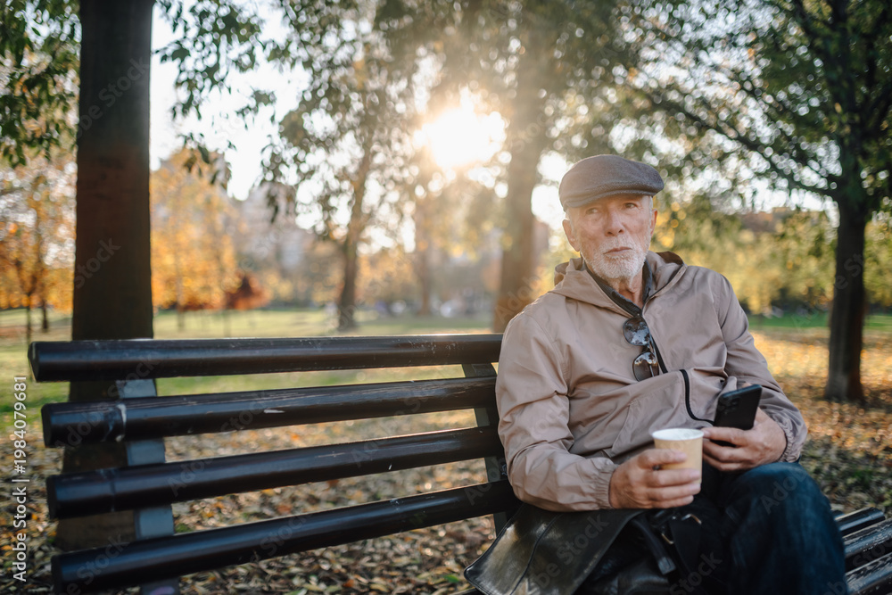 Fototapeta premium Senior man relaxing on park bench enjoying coffee and autumn day