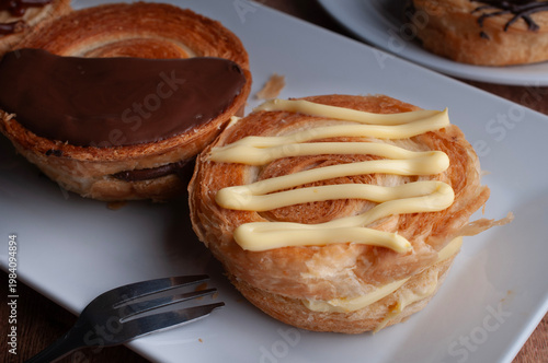 Reposteria casera, pan de hojaldre sobre un plato blanco para disfrutar en familia con cafe o leche, cubierta d vainilla y tenedor al lado.