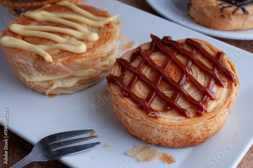 Reposteria casera, pan de hojaldre sobre un plato blanco para disfrutar en familia con cafe o leche, con lineas de cajeta y un tenedor al lado