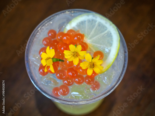A colorful cocktail filled with ice, garnished with herbs and flowers, is placed on a table.
