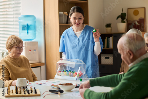 Fotografie Young adult female caregiver leading bingo activity with seniors in care center, supporting cognitive engagement and social interaction