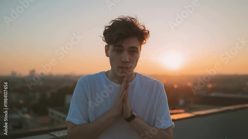 Young casual man with brown hair in white shirt standing on urban rooftop during golden hour sunset