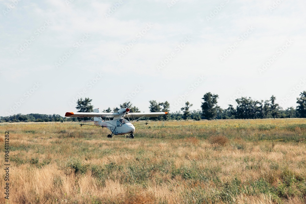 Fototapeta premium crop duster airplane rolling on dirt runway in open farmland landscape under sunlight with empty space for text panoramic banner scene, agribusiness, aviation, rural economy