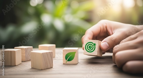 Hand Placing Wooden Block with Target Icon Next to Green Leaf Icon for Sustainable Business Goals and Environmental Growth Concept