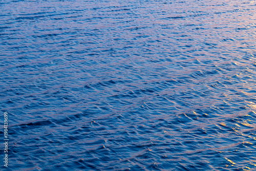 Foto Blue Water Surface with Gentle Ripples and Sunset Reflections,A high-angle, full