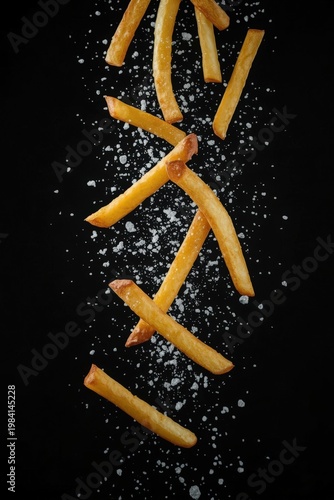 Fries on a black surface with salt sprinkled around them at a kitchen table