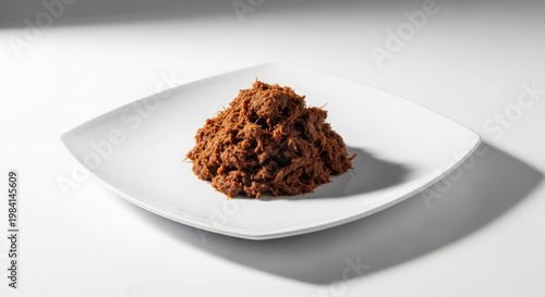 Close up of shredded food on a square white plate against white backdrop