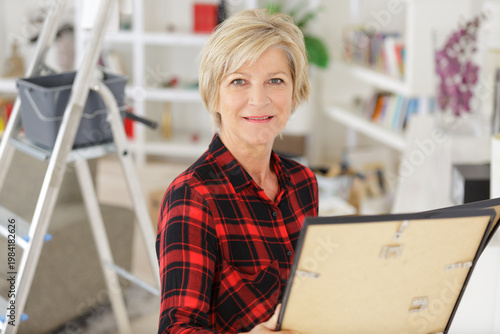 Photos mature woman looking at pisture frame while redecorating