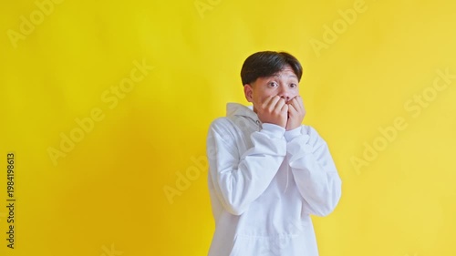 Scared young man expressing fear and trepidation in yellow backdrop