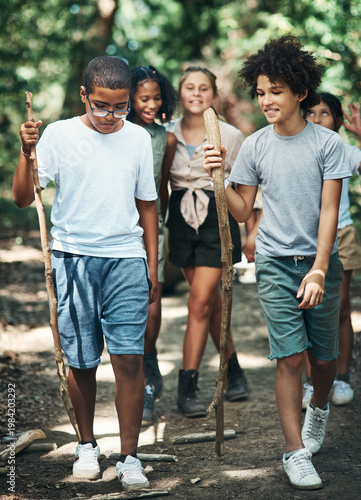 Obraz na plátně Boy, group and stick on walk at summer camp with smile, conversation and adventure in woods