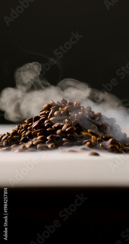A pile of roasted coffee beans emits gentle steam, creating a rich, aromatic atmosphere against a dark background. Shallow depth of field highlights texture and warmth