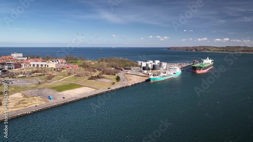 Aerial footage of quayside and industrial oil terminal located along coastline with large storage tanks, docked tanker ships. Industrial oil terminal and tanker ships at port, Fredericia, Denmark