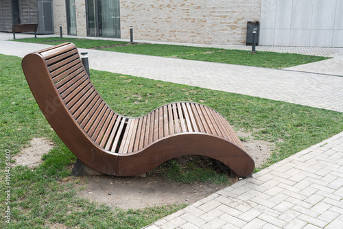 Wallpaper Mural Waveshaped Wooden Bench Near Modern Building, Flowing Slatted Profile Integrates With Paved Walkway And Lawn, Minimalist Aesthetic Complements Architecture While Offering Ergonomic Rest Spot Torontodigital.ca