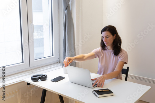 Wallpaper Mural Young woman with long brown hair working on laptop at a bright desk, surrounded by modern decor, showcasing a productive home office environment with natural light Torontodigital.ca
