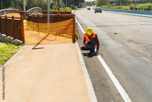 Construction worker inspecting road surface with tablet near safety barrier