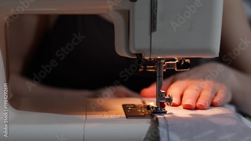 Close-up of hands skillfully guiding blue fabric through a sewing machine. The precise, smooth stitching highlights craftsmanship and careful attention to detail throughout the process.