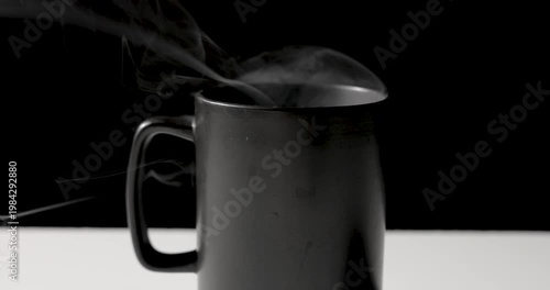 A close-up of a matte black mug with soft steam rising against a dark background, creating a moody, minimal still life with subtle highlights and copy space