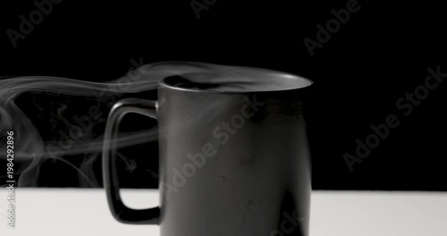 A close-up of a matte black mug with soft steam rising against a dark background, creating a moody, minimal still life with subtle highlights and copy space