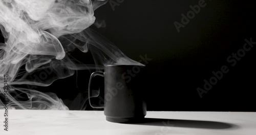 A matte black mug emits swirling white steam against a dark background, lit with dramatic contrast on a minimal surface, creating a moody, atmospheric scene with copy space