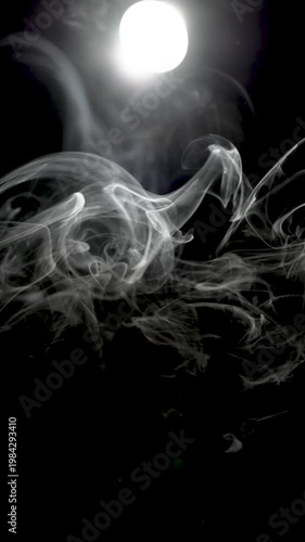 Delicate white smoke forms intricate swirling patterns illuminated by a bright backlight against a dark background, creating a dramatic abstract scene with strong contrast and copy space