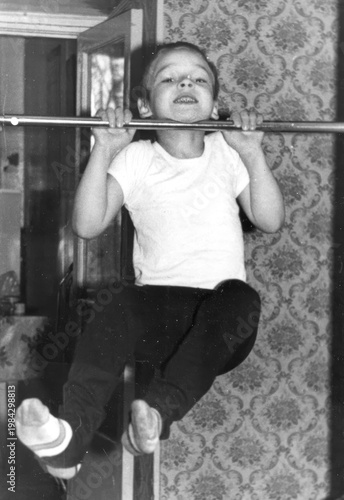 Obraz na plátně Young boy in white t-shirt doing pull-up on horizontal bar mounted in doorframe