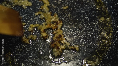 Chopped onions sautéing in frying pan with oil, stirred with wooden spoon. Cooking process, kitchen food preparation, close-up culinary scene.