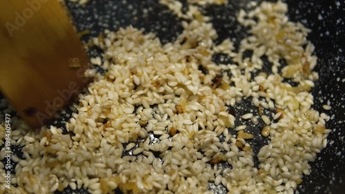 White rice being sautéed in pan for risotto. Cooking process, kitchen close-up, stirring grains in oil, Italian cuisine preparation.