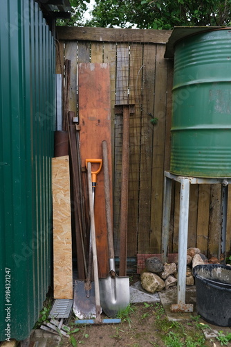 Metal wheelbarrow filled with green garden waste and weeds standing next to a plastic compost bin.