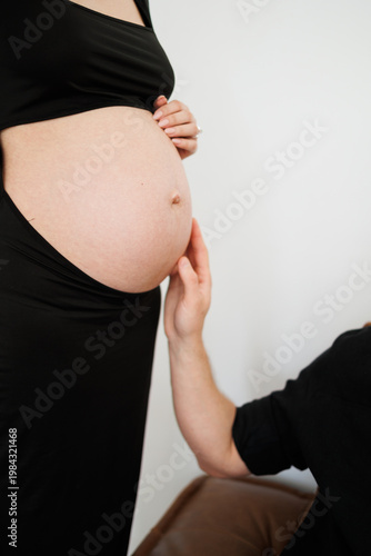 Pregnant woman gently holding her baby bump while embracing her husband in a studio cyclorama setting. Intimate and tender moment between expecting parents, expressing love, care, and anticipation. 