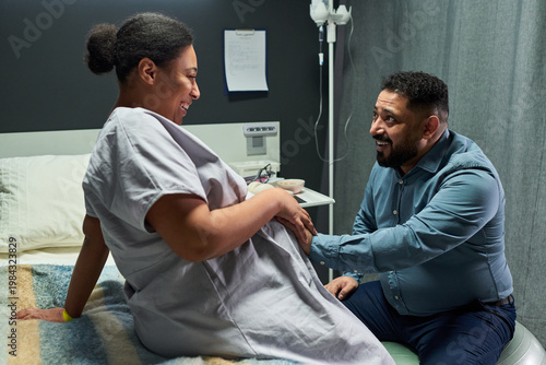 Foto Pregnant woman sitting on hospital bed, partner touching belly and smiling during maternity visit